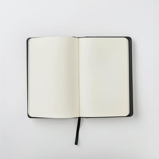 The Example product is an open black notebook with blank white pages and a black ribbon bookmark, shown from above on a plain white background.